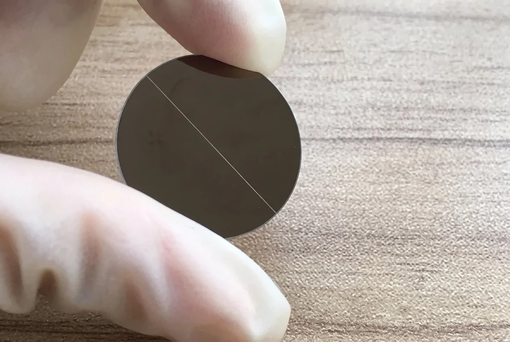 Gloved hand holding a dark coated circular glass plate with one clear slit line
