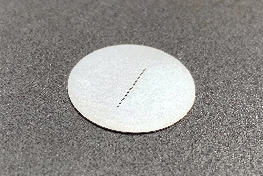 Circular glass slit plate with a fine opaque slit line on a frosted white substrate